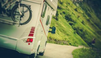 Camper Van on the Road. Class C Motorhome Coach with Bikes on the Rear Side Bike Rack. Family RV Travel.